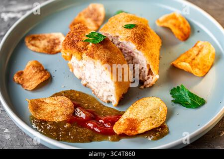 Hühnchen gefüllt mit Speck und Käse, gebraten in Lision. Ein traditionelles französisches Gericht Cordon bleu auf einem blauen Teller. Nahaufnahme. Hochwertige Fotos Stockfoto