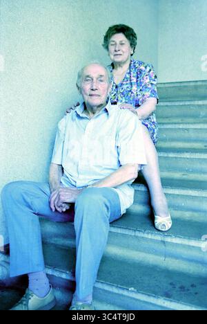 Familie Terol heiratete 65 Jahre, 29-07-1999 Whizgle News, Dutch Desk, Niederlande, 1950-2000 ein älteres Ehepaar sitzt zusammen auf einer Treppe, wobei der Mann nachdenklich in die Kamera schaut, während die Frau liebevoll ihre Hände auf den Schultern legt, beide teilen einen Moment der Wärme und Gesellschaft. Stockfoto