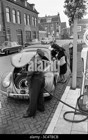 Eröffnung Schmier-/Tankstelle GULF, Brinkmann Haarlem, Eröffnung, Öffnungen, Inbetriebnahme, 26-11-1960 Whizgle News, Dutch Desk, Niederlande, 1950-2000 an einer Tankstelle wird ein Oldtimer betankt, während ein Mechaniker den Motor inspiziert, während eine Frau in der Nähe mit Taschen steht. Im Hintergrund schaffen mehrere klassische Autos und Gebäude eine charmante urbane Szene. Stockfoto
