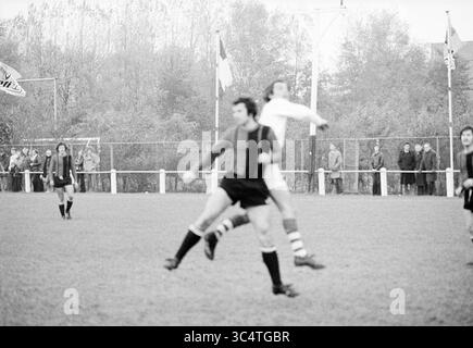 VSV - Kennemeren, Voetbal V.S.V., Velsen, Stormvogels, 02-11-1975 Whizgle News, Dutch Desk, Niederlande, 1950-2000 zwei Fußballspieler treten während eines intensiven Spiels in der Luft um den Ball an, während die Zuschauer von der Seitenlinie aus zusehen. Die Szene fängt die Energie und die Leichtathletik des Spiels vor einem Hintergrund von Bäumen und Zuschauern ein. Stockfoto