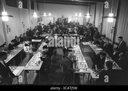 Five Ladies from Hoogoven Chess Tournament - Leser IJmuider Courant, Chess, 22-01-1965 Whizgle News, Dutch Desk, Niederlande, 1950-2000 in einer geräumigen Halle mit zahlreichen Tischen, an denen sich die Teilnehmer intensiv auf ihre Spiele konzentrieren, findet Ein lebhaftes Schachturnier statt. Spieler jeden Alters und Hintergrunds treten in strategische Schlachten ein, wobei Zuschauer die sich abzeichnenden Aktionen beobachten und eine lebhafte Atmosphäre der Konzentration und des Wettbewerbs schaffen. Helle Deckenleuchten beleuchten die Szene und heben die komplizierten Schachbretter und die Intensität der Spieler hervor. Stockfoto