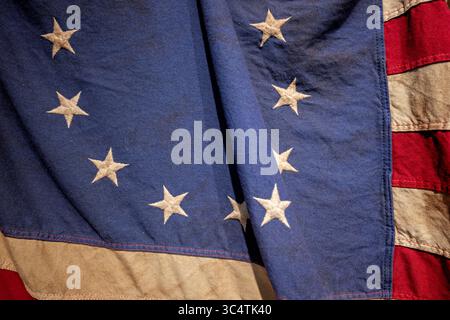 VEREINIGTE STAATEN — Eine detaillierte Ansicht einer Reproduktion der historischen 13-Sterne-amerikanischen Flagge, die allgemein als Betsy Ross-Flagge bekannt ist, zeigt die charakteristische kreisförmige Anordnung von Sternen, die die ursprünglichen 13 Kolonien repräsentieren. Diese Flagge wurde am 14. Juni 1777 vom Kontinentalkongress offiziell angenommen, wodurch die erste offizielle Flagge der Vereinigten Staaten von Amerika eingeführt wurde. Das kreisförmige Muster weißer Sterne auf dem blauen Kanton (links oben) ist eines von mehreren Arrangements, die während des Unabhängigkeitskriegs verwendet wurden, obwohl historische Beweise darauf hindeuten, dass die Sterne häufiger arra waren Stockfoto