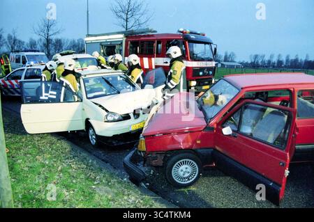 Unfall, Vondellaan, Haarlem, Vondellaan, Niederlande, 12-01-2003 Whizgle News, Dutch Desk, Niederlande, 1950-2000 Notfallhelfer kümmern sich um einen Autounfall mit zwei Fahrzeugen, von denen eines an der Front schwer beschädigt wurde. Feuerwehrleute und medizinisches Personal unterstützen aktiv die Beteiligten und bewerten die Situation, während in der Nähe Einsatzfahrzeuge stationiert sind. Bäume säumen den Hintergrund, was auf eine ländliche Umgebung hinweist. Stockfoto