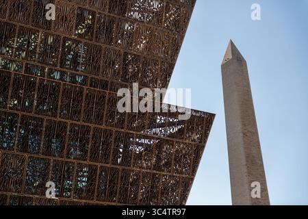 National Museum of African American History and Culture Fassade Washington DC // WASHINGTON DC – die bronzefarbene, filigrane Fassade des Smithsonian National Museum of African American History and Culture bietet einen Blick auf das Washington Monument. Das Außenmaterial des Museums besteht aus 3.600 dekorativen Aluminiumplatten mit bronzefarbener PVDF-Oberfläche, die die Tradition der Eisenhütte versklavter und befreiter afroamerikanischer Handwerker aus dem amerikanischen Süden widerspiegelt, die vor allem in Charleston und New Orleans zu finden sind. Das unverwechselbare dreistöckige Corona-Design des Gebäudes ist vom traditionellen Yoruba cr inspiriert Stockfoto