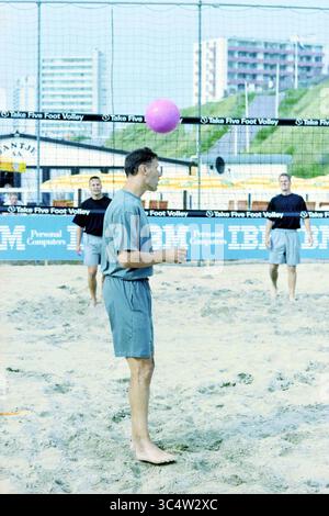 Football Volleyball, Marco van Basten, Zandvoort, Zandvoort, 03-07-1997 Whizgle News, Dutch Desk, Niederlande, 1950-2000 Eine Gruppe von Männern genießt eine Runde Fußvolley auf dem Sand, wobei ein Spieler bereit ist, einen rosafarbenen Ball zu schlagen. Die Atmosphäre ist lebhaft, geprägt von ihrer lässigen Kleidung und der Kulisse von Gebäuden und einem Beachvolleyballnetz. Stockfoto