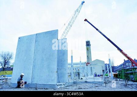 Bau des Stadtbüros, IJm., IJmuiden, Niederlande, 11-12-1994 Whizgle News, Dutch Desk, Niederlande, 1950-2000 Bauarbeiter bedienen schwere Maschinen auf einer Baustelle, auf der große Betonplatten installiert werden. Kräne ragen darüber und heben strukturelle Elemente an, während ein Arbeiter den Vorgang von vorne aus beobachtet. Stockfoto