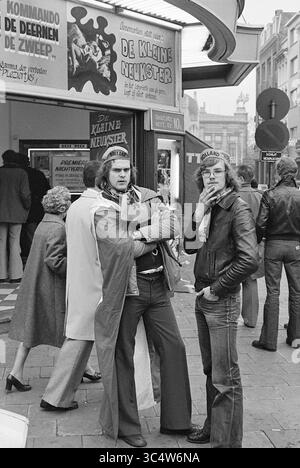 Fußballparty Keyserlei Antwerpen mit niederländischen Fans, Football Netherlands, 26-03-1977 Whizgle News, Dutch Desk, Niederlande, 1950-2000 zwei junge Männer mit unverwechselbaren Hüten und Mode aus der Zeit stehen selbstbewusst vor einem Kinoeingang. Sie posieren mit überkreuzten Armen und wirken entspannt, aber engagiert in ihrer Umgebung. Im Hintergrund entfaltet sich eine belebte Straßenszene mit Fußgängern und einem Filmplakat, das oben deutlich zu sehen ist. Stockfoto