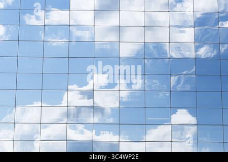 Glasgebäude mit Himmelsspiegelung. Moderne Architekturfassade mit Wolken in Fensterpaneelen. Städtisches Business Center, Außenansicht. Blauer Himmel gespiegelt. Stockfoto