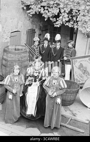 Wine Festival Unkel, Deutschland, Wine, 09-10-1977 Whizgle News, Dutch Desk, Niederlande, 1950-2000 Eine Gruppe von Personen in historischen Kostümen posiert vor Holzfässern, mit einigen Bechern. Hervorzuheben ist eine Frau in einem aufwendigen Kleid, flankiert von drei Mädchen in passenden Outfits. Im Hintergrund stehen mehrere Männer in formeller Kleidung, darunter Hüte, mit einer Flagge. Die Szene fängt eine festliche oder zeremonielle Atmosphäre ein. Stockfoto