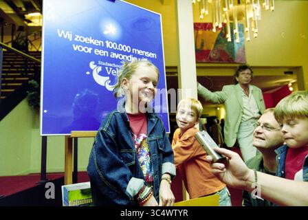 100.000 Besucher Velsen Theater, Velsen, 06-06-2002 Whizgle News, Dutch Desk, Niederlande, 1950-2000 Eine Gruppe von Kindern steht vor einem großen Schild, das die Teilnehmer zu einer Veranstaltung einlädt, während ein Erwachsener aus dem Hintergrund beobachtet. Die Kinder scheinen aufgeregt zu sein, ein Mädchen lächelt hell in die Kamera, alle engagiert und neugierig auf den Anlass. Stockfoto