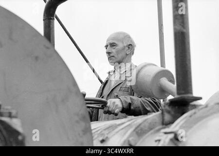 Schwimmkran Fa Figee + HR Nelis, Figee, Krane, Haarlem, Niederlande, 03-04-1981 Whizgle News, Dutch Desk, Niederlande, 1950-2000 Ein Mann steht entschlossen am Steuer eines alten Traktors, sein verwittertes Gesicht spiegelt jahrelange Erfahrung wider. Mit einem Arbeitshemd greift er das Lenkrad zielgerichtet, konzentriert sich auf die vor ihm liegende Aufgabe und verkörpert den Geist der landwirtschaftlichen Arbeit. Stockfoto