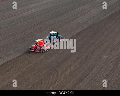 Aus der Vogelperspektive eines Traktors mit einer roten Sämaschine, der auf einem riesigen, frisch bearbeiteten Feld arbeitet und dunkle, gemusterte Wege in der brandenburgischen Landschaft, Bralitz, Brandenburg, hinterlässt. Stockfoto