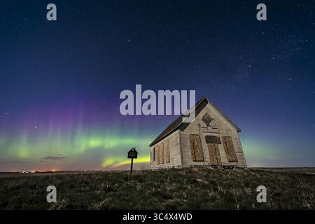 23. Mai 2018 – Alberta, Kanada – das 1910 Liberty Schoolhouse, eine klassische 1-Zimmer-Schule in der Prärie von Alberta unter dem Sternenhimmel in einer Frühlingsnacht, in der eine aurora nach Norden tanzt. Mondlicht sorgt für die Beleuchtung. Cassiopeia ist über der Schule. Polaris ist ganz oben... Dies ist eine Mischung aus einem Stapel von 4 Belichtungen für den Boden, um Geräusche zu glätten, und einer einzigen Belichtung für den Himmel, mit einem Vintage-Effekt, der Luminar auf den Boden aufträgt, um den rustikalen Ton zu erhalten. Mit dem Laowa 15-mm-Objektiv und der Sony a7III Kamera. Alle 20 Sekunden bei f/2,8 und bei ISO 800 und als Teil einer 360-Frame-Zeitraffer aufgenommen Stockfoto