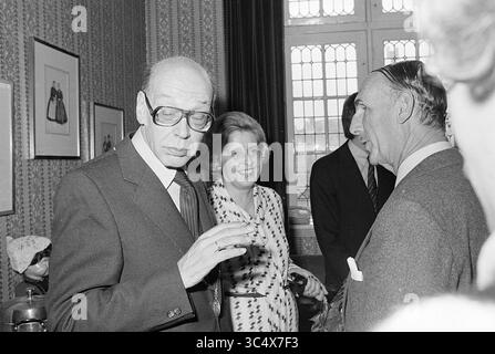 Installation von Bürgermeister Machielsen Zandvoort, Bürgermeister, 05-10-1977 Whizgle News, Dutch Desk, Niederlande, 1950-2000 Eine Gruppe von Personen, die sich mit einem Mann unterhalten, der seine Brille anpasst und nachdenklich wirkt, während eine Frau freundlich lächelt. Die Einrichtung verfügt über dekorative Wände und gerahmte Kunstwerke, die zu einer formellen Atmosphäre beitragen. Stockfoto