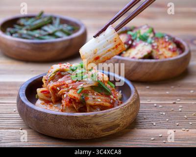 Ein Nahaufnahme-Foto von Essstäbchen, um ein Napa-Kohl-Stück Kimchi aus einer hölzernen Schüssel zu holen. Stockfoto