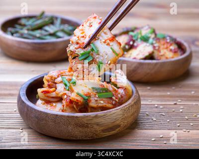 Ein Nahaufnahme-Foto von Essstäbchen, um ein Napa-Kohl-Stück Kimchi aus einer hölzernen Schüssel zu holen. Stockfoto