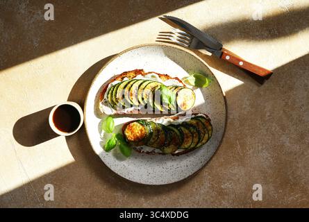 Köstliche Bruschetta mit Ricotta, gegrillter Zucchini und Kräutern auf einem Teller auf Holztisch in hartem Sonnenlicht, Blick von oben Stockfoto