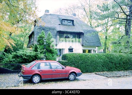 Reetdachhaus, Krullenlaan 27, Bloemendaal, Krullenlaan, 06-11-1997 Whizgle News, Dutch Desk, Niederlande, 1950-2000 Ein charmantes Strohdach-Cottage ist von üppigem Grün und bunten Herbstblättern umgeben. Ein rotes Auto parkt entlang des Steinweges und ergänzt die gemütliche und einladende Atmosphäre der Szene. Stockfoto