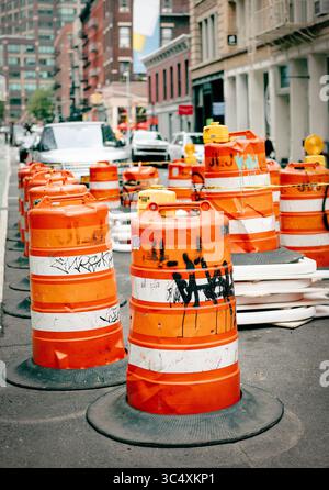 Orangene Verkehrsfässer säumen eine geschäftige Stadtstraße und führen Fahrzeuge am 16. Mai 2025 durch ein Baugebiet in New York City, NY, USA. Stockfoto