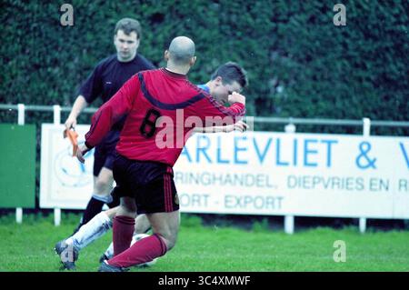 Fußball: Stormvogels - AFC, IJmuiden, Niederlande, 10-03-2001 Whizgle News, Dutch Desk, Niederlande, 1950-2000 Ein Fußballspieler in einem roten Trikot mit der Nummer 8 spielt in einem Wettkampf, während ein anderer Spieler in Schwarz aus dem Hintergrund beobachtet. Die Szene fängt die Intensität des Spiels ein, mit einem grasbewachsenen Feld und einem Banner in der Ferne, das ein lokales Unternehmen kennzeichnet. Stockfoto