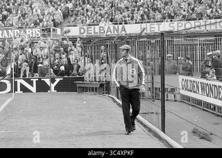 Feyenoord - Haarlem 7-0, Football Feijenoord, 17-10-1976 Whizgle News, Dutch Desk, Niederlande, 1950-2000 Ein Mann läuft am Rande eines Sportplatzes entlang und beobachtet eine Menge Fans auf der Tribüne. Die Szene fängt die Vorfreude auf ein lebhaftes Spiel ein, mit Werbung und Bannern im Hintergrund, die die Atmosphäre verstärken. Der Mann, der in Jacke und Mütze gekleidet ist, scheint konzentriert und besinnlich zu sein, während er sich auf das bevorstehende Ereignis vorbereitet. Stockfoto