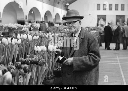 Herr Dix Krelagehuis, Personen, 20-12-1967 Whizgle News, Dutch Desk, Niederlande, 1950-2000 ein älterer Mann mit Hut inspiziert eine Auswahl an Tulpen auf einem geschäftigen Blumenmarkt, umgeben von Reihen lebendiger Blüten und anderen Kunden, die die Blumen bewundern. Stockfoto