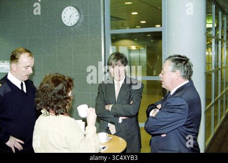 Fire at Schiphol, Schiphol, 17-01-2001 Whizgle News, Dutch Desk, Niederlande, 1950-2000 Eine Gruppe von vier Personen führt ein Gespräch und steht an einem kleinen Tisch. Sie scheinen etwas Ernstes zu diskutieren, wobei zwei von ihnen ihre Arme kreuzen, während sie aufmerksam zuhören. Das Ambiente bietet eine moderne, offene Umgebung mit großen Fenstern und einer Uhr an der Wand, die die Zeit anzeigt. Stockfoto