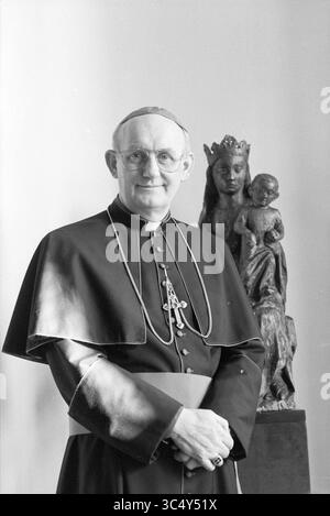 Bischof Bomers, Römisch-Katholische Kirche, 23-02-1989 Whizgle News, Dutch Desk, Niederlande, 1950-2000 Ein Geistlicher steht selbstbewusst in traditioneller kirchlicher Kleidung, mit einem markanten cape und einer Kreuzkette. Hinter ihm fügt eine Statue der Madonna und des Kindes dem Schauplatz ein spirituelles Element hinzu, das die Vermischung von Glauben und Kultur hervorhebt. Stockfoto
