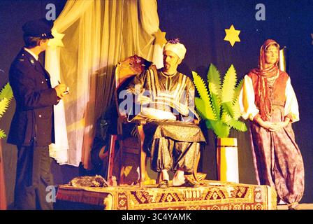Theater Bernard Alfrink School, Santpoort, Santpoort, 04.12-1995 Whizgle News, Dutch Desk, Niederlande, 1950-2000 Eine Szene aus einer Theateraufführung mit einer königlichen Figur auf einem kunstvollen Stuhl, die in traditioneller Kleidung verziert ist, während zwei Charaktere sich mit ihm auseinandersetzen – einer in Uniform und der andere in kultureller Kleidung, vor einem Hintergrund von Sternen und Laub. Stockfoto