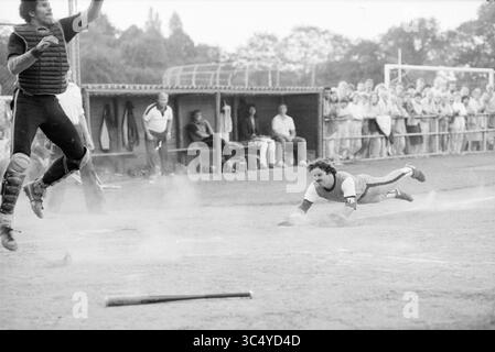 Bloemendaal - Kennemerland, MEN, Softball, 18-08-1984 Whizgle News, Dutch Desk, Niederlande, 1950-2000 Ein Baseballspieler rutscht dramatisch in Richtung Heimplatte, während der Fänger sich darauf vorbereitet, ihn zu markieren. Im Hintergrund beobachtet eine Menschenmenge aufmerksam, wobei die Teamkollegen in einer Ausbuchtung in der Nähe sitzen, was die Spannung des Augenblicks erhöht. Staub steigt vom Feld auf, was die Intensität der Action unterstreicht. Stockfoto