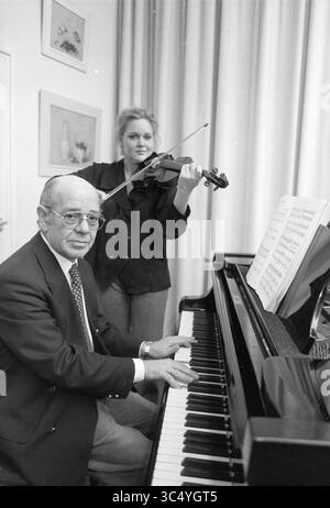 Herr de Groot mit Tochter, Haarlem, Niederlande, 12-11-1991 Whizgle News, Dutch Desk, Niederlande, 1950-2000 Ein Mann sitzt an einem Flügel und spielt, während eine Frau hinter ihm steht und geschickt Geige spielt. Die Noten sind vor dem Pianisten offen und schaffen eine Atmosphäre der Zusammenarbeit in der Musik. Stockfoto