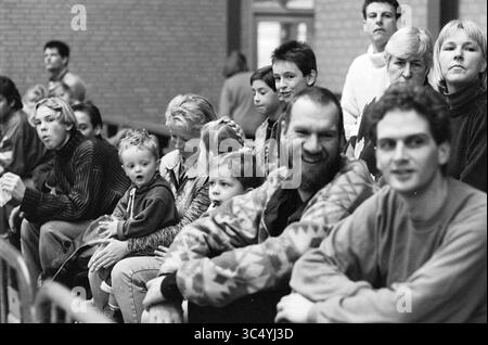 Publikum bei den Straßenmannschaften des Hallenfußballturniers Velserbroek, 17-01-1997 Whizgle News, Dutch Desk, Niederlande, 1950-2000 Eine Gruppe unterschiedlicher Personen, darunter Kinder und Erwachsene, sitzt eng zusammen und zeigt eine Reihe von Ausdrucksformen von Neugier bis Zufriedenheit. Die Szene fängt einen Moment der gemeinsamen Erfahrung ein, wahrscheinlich in einem gemeinschaftlichen oder sozialen Umfeld. Stockfoto
