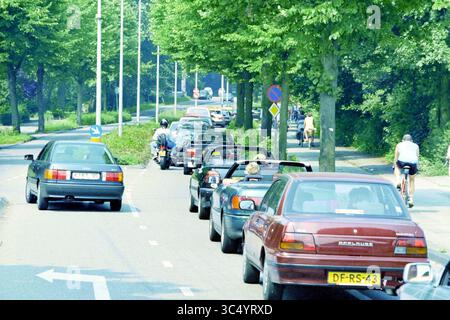 Verkehrsstaus nach Zandvoort, Zandvoort, 29-07-1995 Whizgle News, Dutch Desk, Niederlande, 1950-2000 Eine geschäftige Straßenszene mit einer Reihe von Autos und Motorrädern, umgeben von üppigen Bäumen. Radfahrer teilen sich die Straße und betonen eine Mischung aus Verkehrsmitteln in einer lebhaften urbanen Umgebung. Stockfoto