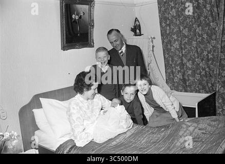 Kinder von Mr. Black, Kinder, Kinder, Kinderheime, Kinderparty, Kinder, 13-04-1964 Whizgle News, Dutch Desk, Niederlande, 1950-2000 Ein freudiger Familienmoment mit einer Mutter, die ein Neugeborenes in einem gemütlichen Schlafzimmer wiegt, umgeben von vier Kindern und einem stolzen Vater. Die Atmosphäre ist voller Spannung und Wärme, während sich alle versammeln, um die Ankunft des neuesten Familienmitglieds zu feiern. Stockfoto
