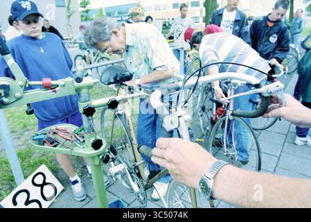Fahrradinspektion Excelsior, 23-07-1996 Whizgle News, Dutch Desk, Niederlande, 1950-2000 Eine Gruppe von Personen, darunter eine Gruppe von Erwachsenen und Kindern, beschäftigt sich mit einer Fahrradreparaturwerkstatt, die sich auf die Anpassung und Reparatur verschiedener Aspekte der Fahrräder konzentriert. Die Hände arbeiten aktiv am Lenker, während andere beobachten und helfen, um eine gemeinsame Atmosphäre zu schaffen. Stockfoto