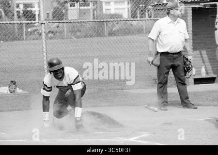 Softball, Kennemerland MEN, 07-08-1992 Whizgle News, Dutch Desk, Niederlande, 1950-2000 Ein Baseballspieler hockt sich in einem staubigen Infield und bereitet sich darauf vor, zu schlagen, während ein Schiedsrichter in der Nähe mit einem fokussierten Ausdruck steht. Die Szene fängt die Intensität des Spiels mit den Zuschauern im Hintergrund ein. Stockfoto