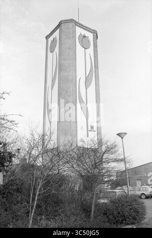 Wasserturm Roelofarendsveen., Wasserturm, Roelofarendsveen, 11-12-1986 Whizgle News, Dutch Desk, Niederlande, 1950-2000 Ein hohes Gebäude mit einem lebendigen Wandgemälde mit stilisierten Tulpen, umgeben von kargem Laub und einer urbanen Umgebung, die eine Mischung aus Natur und künstlichen Elementen zeigt. Stockfoto