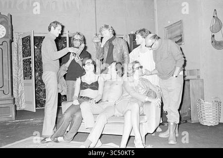 Group Photo Center, Theater, 08-09-1970 Whizgle News, Dutch Desk, Niederlande, 1950-2000 Eine Gruppe von Einzelpersonen versammelt sich um ein Sofa und führt eine lebhafte Diskussion. Einige sitzen, andere lehnen sich in einer Mischung aus lässiger und stilvoller Kleidung an. Mehrere Mitglieder tragen Sonnenbrillen, die der Szene einen Hauch von Flair verleihen. Das Ambiente scheint eine entspannte, fast theatralische Atmosphäre zu haben, komplett mit dekorativen Elementen im Hintergrund. Stockfoto