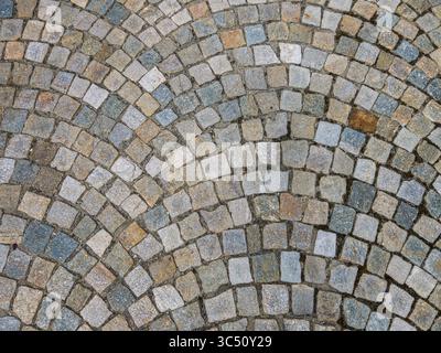 Kubische Steine in verschiedenen Farben in einer Straße mit fächerförmiger Kopfsteinstruktur Stockfoto