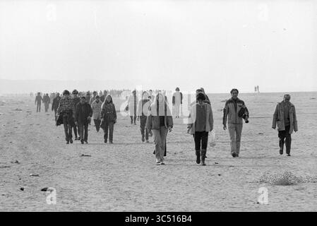 Beach Walk Haarlems Dagblad, Haarlems Dagblad etc. Und IJmuider Courant and Koeri, Walking, 31-07-1980','15-02-1981 Whizgle News, Dutch Desk, Niederlande, 1950-2000 Eine große Gruppe von Menschen läuft stetig am Strand entlang, ihre Figuren sind vor einem trüben Horizont geschildert und schaffen ein Gefühl kollektiver Bewegung und Reflexion. Stockfoto