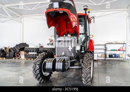 Neuer Traktor mit offener Motorhaube in einer hellen, modernen Werkstatt für Motordiagnose, Maschinenwartung und Inspektion landwirtschaftlicher Geräte. Stockfoto