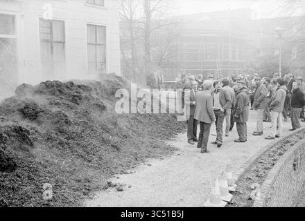 Transfer der Baumrinde von Milieudefensie, Hillegom, Bomen, Hillegom, 29-02-1984 Whizgle News, Dutch Desk, Niederlande, 1950-2000 Eine Menschenmenge versammelt sich in der Nähe eines großen Hügels aus Erde, möglicherweise Mutterboden oder Kompost, außerhalb eines Gebäudes. Einige Personen führen Gespräche, während andere den Tatort beobachten. In der Nähe sind Baugerüste sichtbar, was darauf hindeutet, dass in diesem Bereich noch Arbeiten durchgeführt werden. Stockfoto