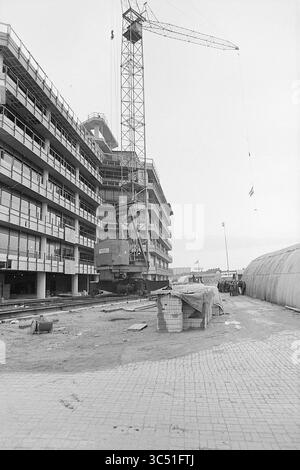 Am höchsten Punkt des Baus von Geschäftsgebäuden, 00-00-1972 Whizgle News, Dutch Desk, Niederlande, 1950-2000 Eine Baustelle mit einem großen Kran, der über einem teilweise fertiggestellten Gebäude thront, mit verstreuten Baumaterialien und Arbeitskräften im Hintergrund. Die Szene fängt das geschäftige Treiben und die Entwicklung der urbanen Architektur ein. Stockfoto