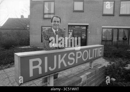 Herr van Oefelen State Police Hillegom, Police, Hillegom, 26-01-1989 Whizgle News, Dutch Desk, Niederlande, 1950-2000 Ein Mann in einem Karomuster lehnt sich beiläufig an ein deutlich gezeigtes Schild mit der Aufschrift „RIJKSPOLITIE“ vor einem modernen Gebäude. Hinter ihm zeigt ein Fenster eine Figur, die den Tatort beobachtet. Die Umgebung lässt eine professionelle oder offizielle Atmosphäre vermuten. Stockfoto