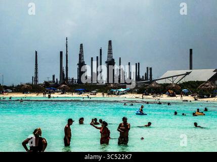 Besucher am Baby Beach in Aruba mit einer verlassenen Ölraffinerie in der Ferne Stockfoto