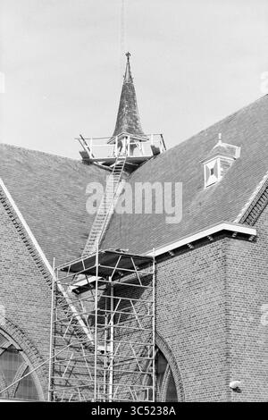 Restaurierung des RC Kirchturms, Hillegom, Monseigneur van Leeuwenlaan, 09-03-1993 Whizgle News, Dutch Desk, Niederlande, 1950-2000 Ein hoher Turm mit einer Wetterfahne ist der Mittelpunkt einer Kirche, die renoviert wird, mit Gerüsten, die den Arbeitern den Zugang zum Oberbau ermöglichen. Das robuste Mauerwerk steht im Kontrast zur komplexen Architektur des Gebäudes und zeigt sowohl handwerkliches Können als auch die laufenden Instandhaltungsarbeiten. Stockfoto