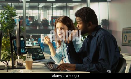 Manager beaufsichtigt die Arbeit des Buchhalters, indem er Finanzdaten auf den PC eingibt und Berichte überprüft. Vorgesetzter, der den Fortschritt eines Mannes überwacht, der im Büro arbeitet und Daten abgleicht, Kamera B Stockfoto