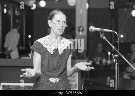 Sonstiges Künstlerfestival Zijlpoort, Gesangschöre, Haarlem, Niederlande, 24-04-1988 Whizgle News, Dutch Desk, Niederlande, 1950-2000 Eine Frau steht an einem Mikrofon und gibt animiert Gesten, während sie mit einem Publikum spricht. Sie trägt ein Vintage-Kleid mit Spitzenkragen, das ein Gefühl von Leidenschaft und Engagement in ihrer Geschichte oder Präsentation vermittelt. Die Atmosphäre lässt eine intime Zusammenkunft mit sanfter Beleuchtung und aufmerksamen Zuhörern im Hintergrund vermuten. Stockfoto
