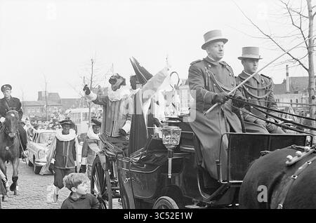 St. Nicholas Eintrag in Haarlem, St. Nicholas, Sinterklaas, 18-11-1964 Whizgle News, Dutch Desk, Niederlande, 1950-2000 Bei Einer Prozession reiten Menschen in aufwendigen Kostümen in einer Pferdekutsche, begleitet von Kindern und einer Menschenmenge. Eine Mischung aus festlicher Kleidung und traditioneller Kleidung trägt zur lebhaften Atmosphäre der Veranstaltung bei. Stockfoto