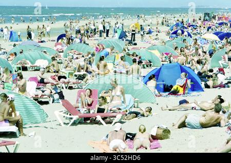 Geschäftiger Strand, Zandvoort, Zandvoort, 12-07-2003 Whizgle News, Dutch Desk, Niederlande, 1950-2000 Eine überfüllte Strandszene voller Sonnenanbeter, die sich unter bunten Sonnenschirmen entspannen, spielen und das warme Wetter genießen, während sich Familien und Freunde auf dem Sand versammeln. Stockfoto